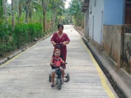 Jalan Rabat Beton TMMD Jadi Tempat Nyaman, Ibu Marisa Momong Anak dengan Sepeda